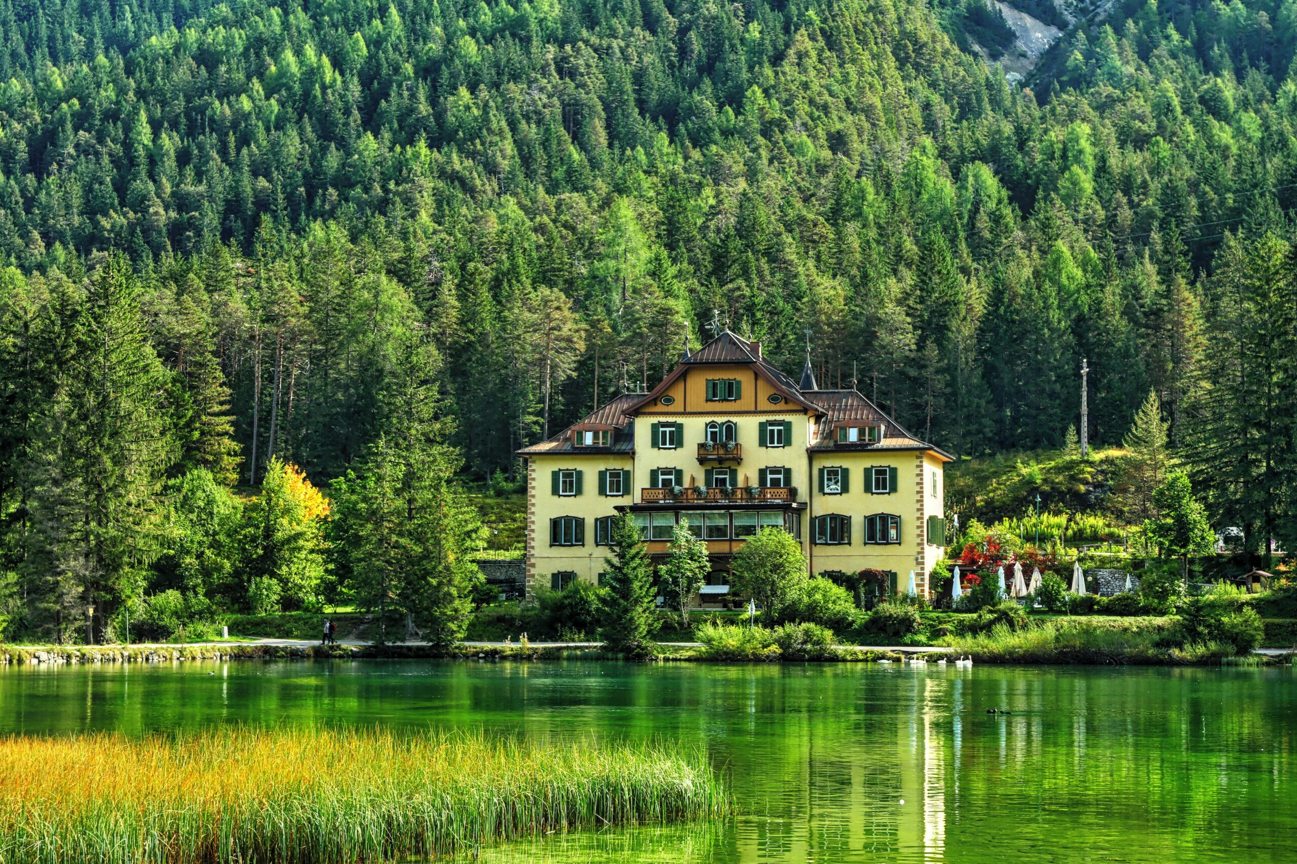 Scenic view of a villa by a tranquil lake surrounded by lush forest in Trentino-Alto Adige, Italy.